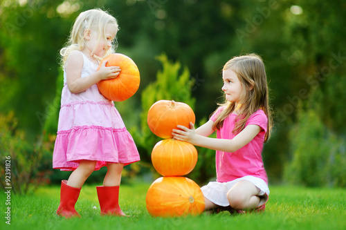 Two little sisters playing with huge pumpkins