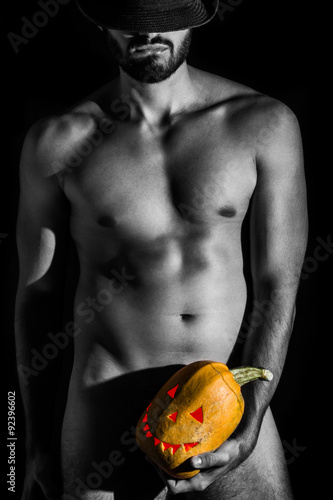 Naked man with hat holding creepy carved halloween pumpkin