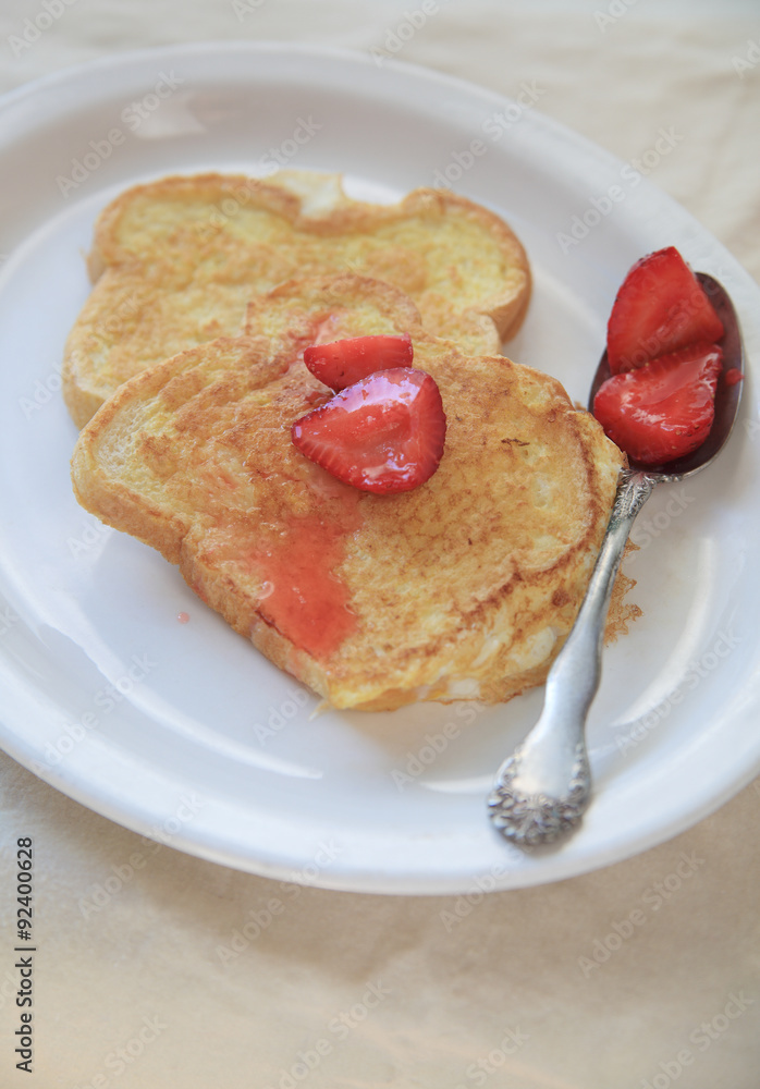 Macerated strawberries spooned over French toast on a white platter Macerated strawberries spooned over French toast on a white platter