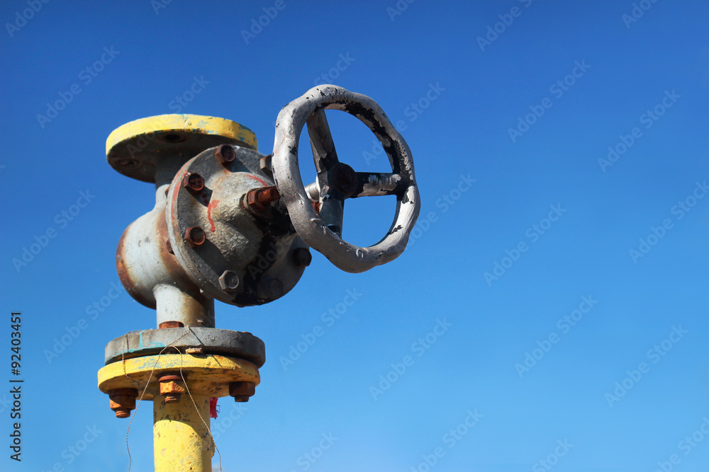 Fototapeta premium Old yellow gas pipe with valve on blue sky background