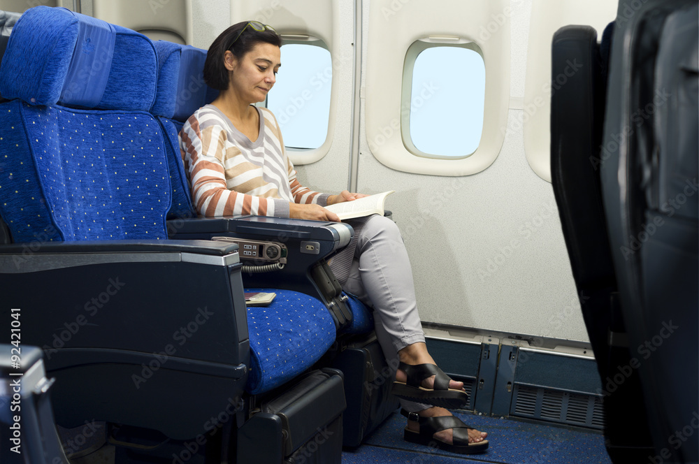 Fototapeta premium caucasian woman passenger in airplane reading a book on the seat