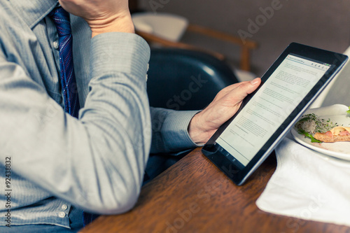 Businessman working on tablet pc during breakfast at home/hotel.