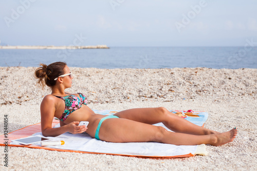 Pretty girl lying on the beach and sunbathing with phone in her hand.