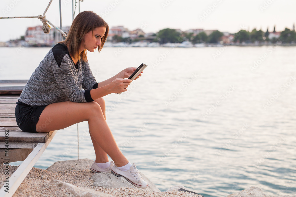 Woman sitting on the bridge and using tablet.