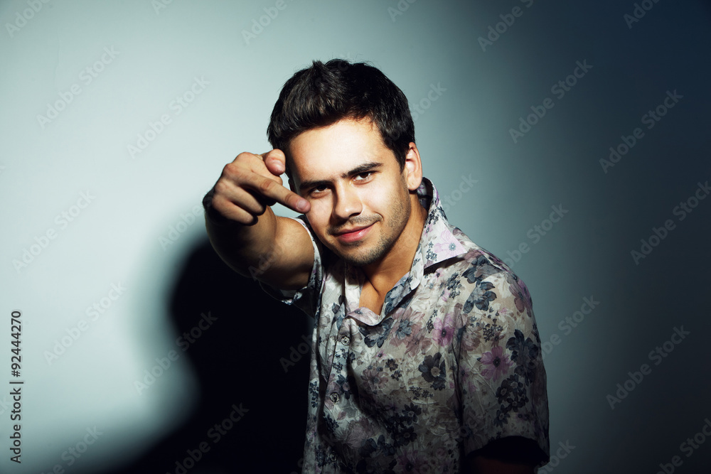 Fototapeta premium Studio portrait of a handsome young man in shirt posing in the spotlight over a grey background and showing middle finger 
