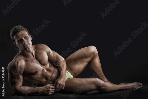 Muscular young bodybuilder laying down in relaxed pose, smiling