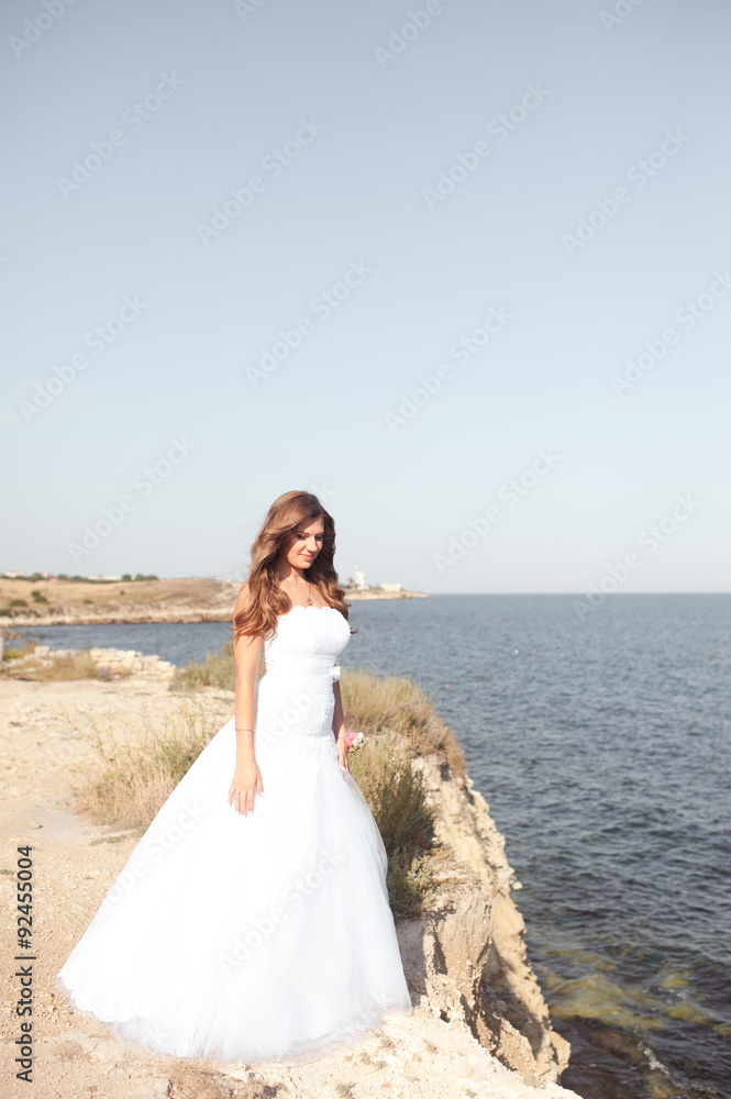 Young beautiful bride posing outdoors. Standing at sea shore. Summer time. Wedding day. Young beautiful bride posing outdoors. Standing at sea shore. Summer time. Wedding day.
