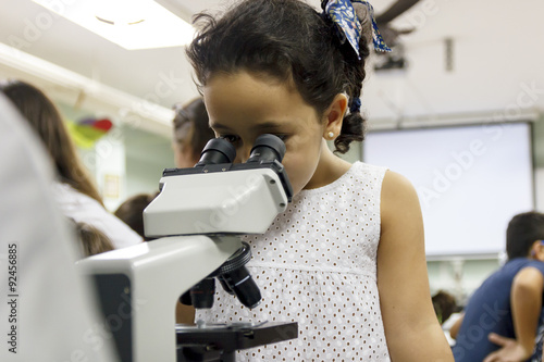 Experimentando en clase de biología. Niños investigando. Niña mirando por el microscopio. Actividad escolar. 