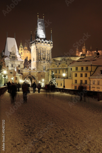 Night colorful snowy Prague gothic Castle with Bridge Tower and St. Nicholas' Cathedral and Sculptures from the Charles Bridge, Czech republic