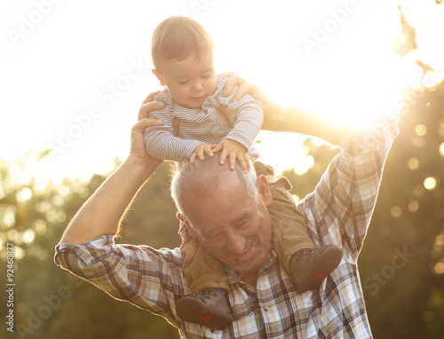Foto Grandfather carrying grandson on shoulders in park on sunny autumn day