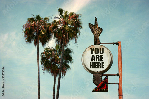 aged and worn vintage photo of you are here sign with palm trees