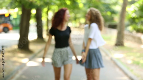 Two beautiful girls walking and laughing at park
