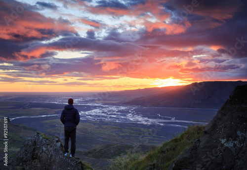 Man standing on a ledge of a mountain, enjoying the beautiful sunset over a wide river valley in Thorsmork, Iceland. 