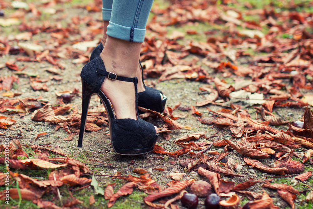 Woman feet in black elegant high heels in autumn leaves