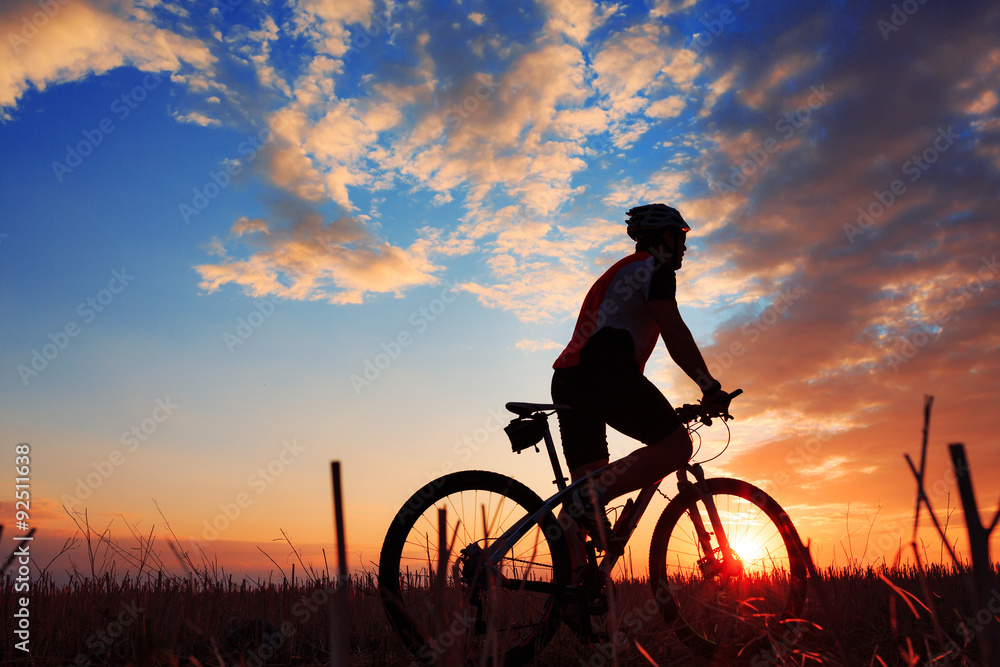 Silhouette of a biker and bicycle on sunset background.