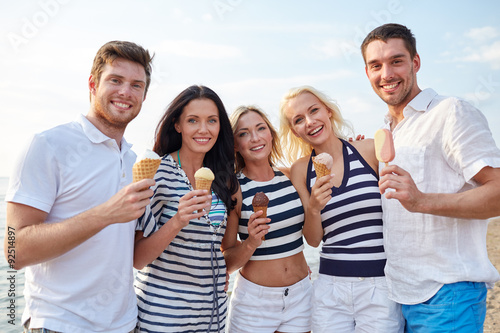 smiling friends eating ice cream on beach