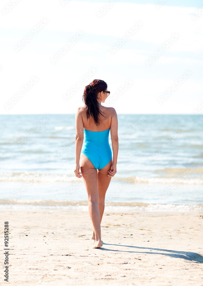 young woman in swimsuit walking on beach