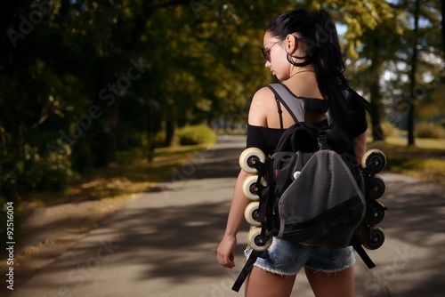 Beautiful girl brunette with backpack behind back in which roller skates