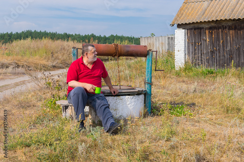 Bearded senior man sitting at country draw-well in central Ukraine