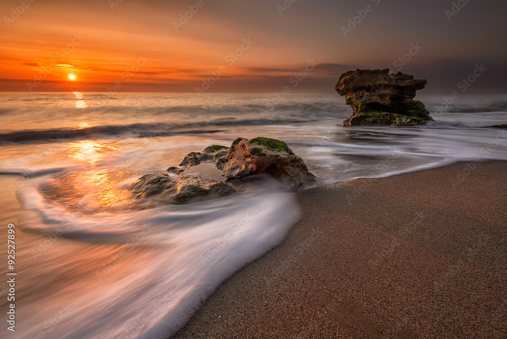 Fototapeta premium Wschód słońca nad morzem. Burzowa plaża z wolną migawką i wypływającymi falami