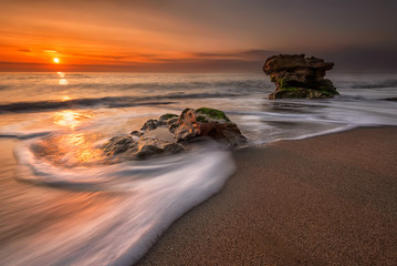 Sea sunrise. Stormy sea beach with slow shutter and waves flowing out
