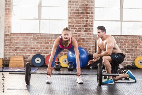 Woman lifting barbell with her trainer at crossfit session