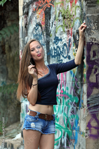 Young woman leaning on a wall with graffity and smoking a cigarette