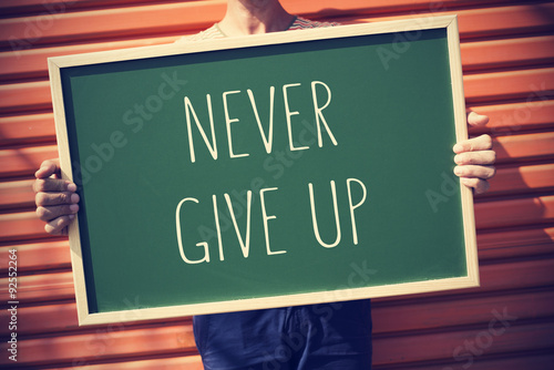 young man with a chalkboard with the text never give up, vignett photo