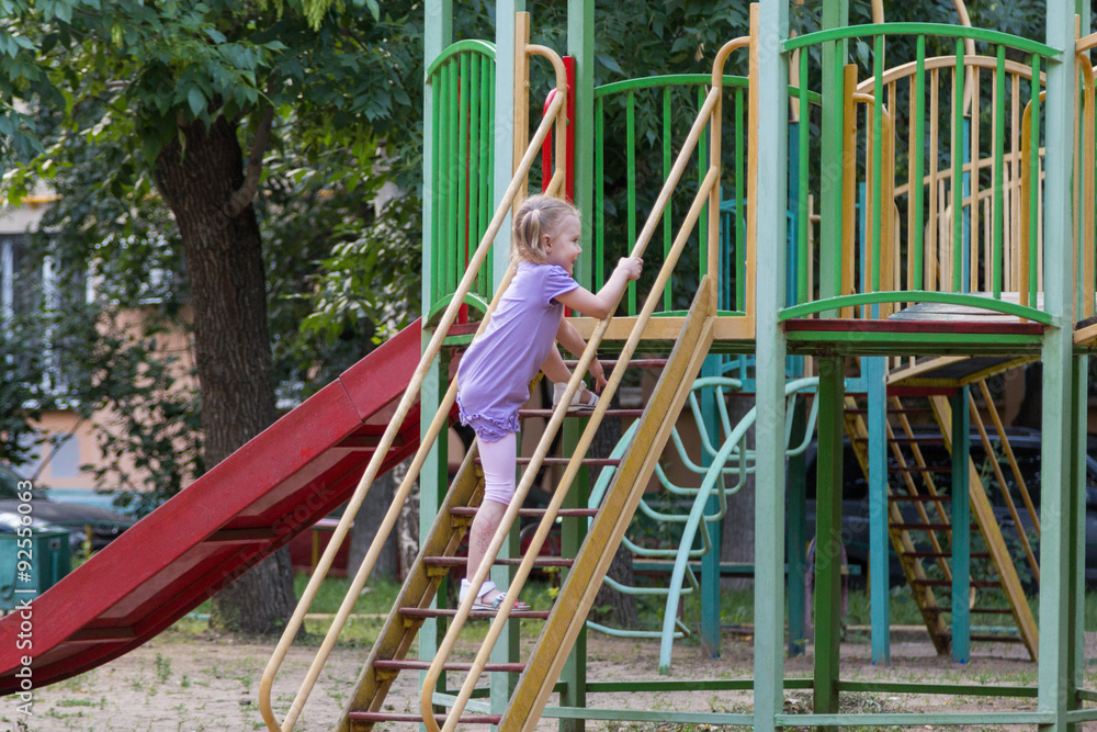 Fototapeta premium little girl with a ponytail climbs the stairs to the slide
