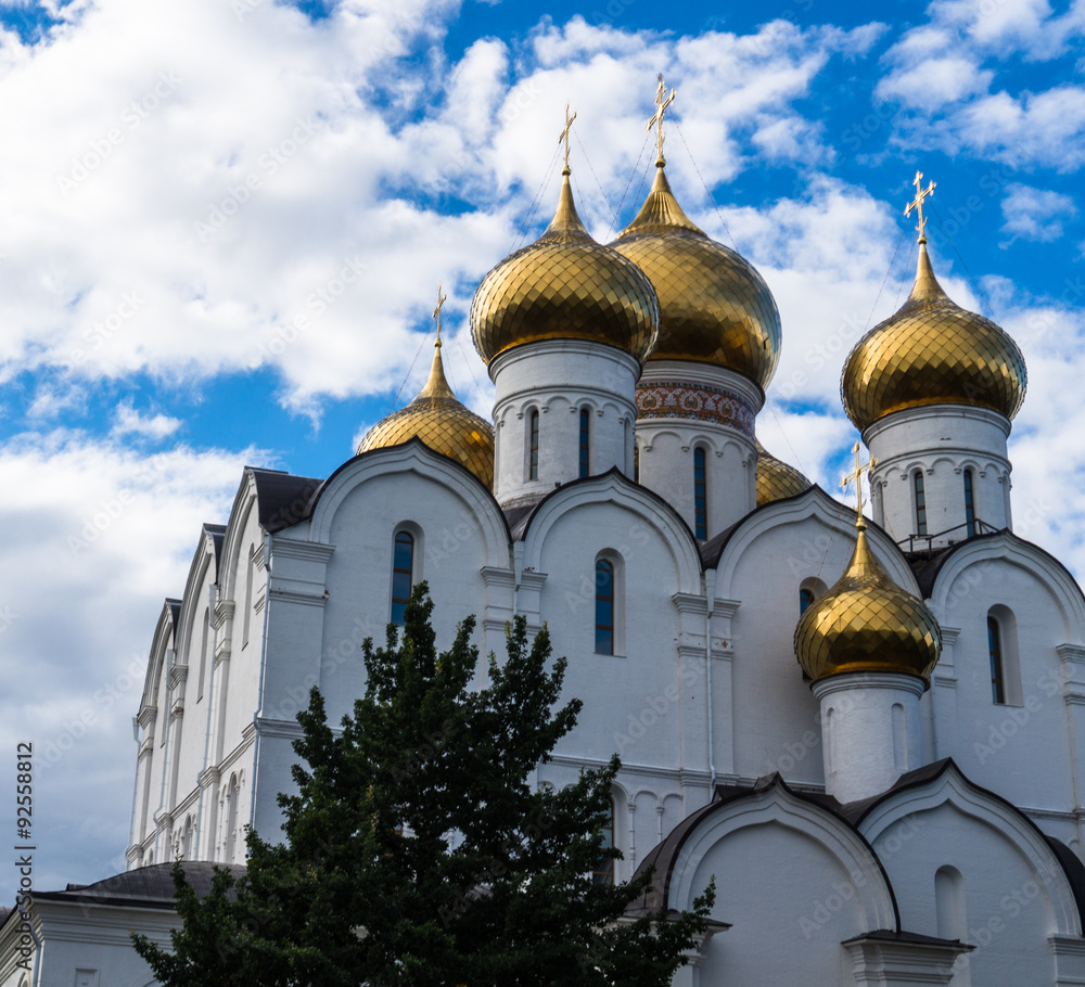 white Cathedral with its golden domes and crosses against blue sky and clouds in Yaroslavl, Russia