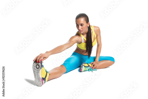 sportswoman warming up her legs sitting on floor on white