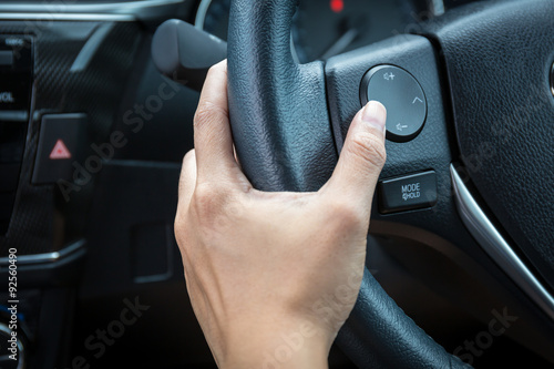 A woman hand pushes the volume control button on a steering wheel. © powerbeephoto