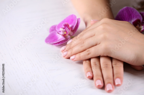 Woman hands with french manicure and orchid flowers on wooden table close-up © Africa Studio