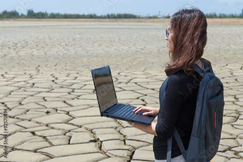 young woman stand on dry soil, earth cracked with laptop
