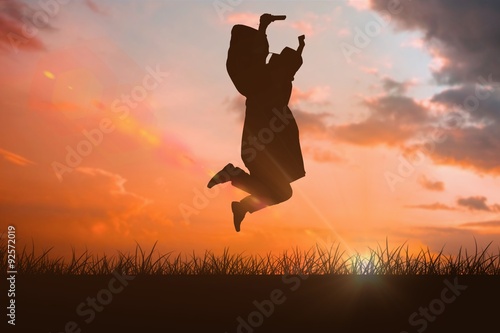 Composite image of happy male student in graduate robe jumping