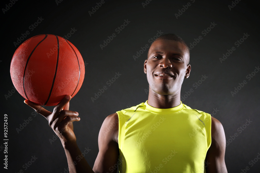 African American basketball player holding ball on dark background