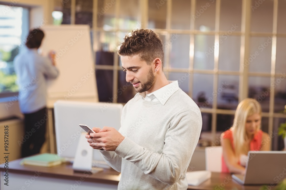 Businessman texting on phone with colleagues working in office Businessman texting on phone with colleagues working in office