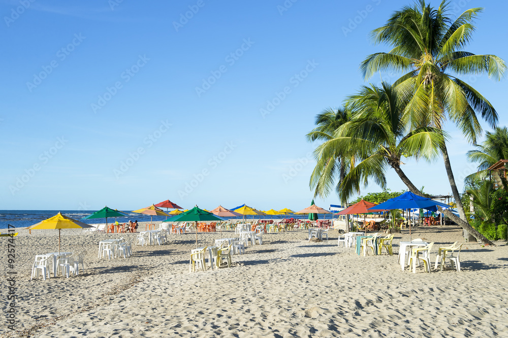 Palm trees stand over rustic village beach with beach chairs and umbrellas on the northeast Nordeste coast of Brazil