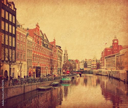 The Singel is one of the numerous canals in Amsterdam, Netherlands . In the background Munttoren . Photo in retro style. Paper texture.