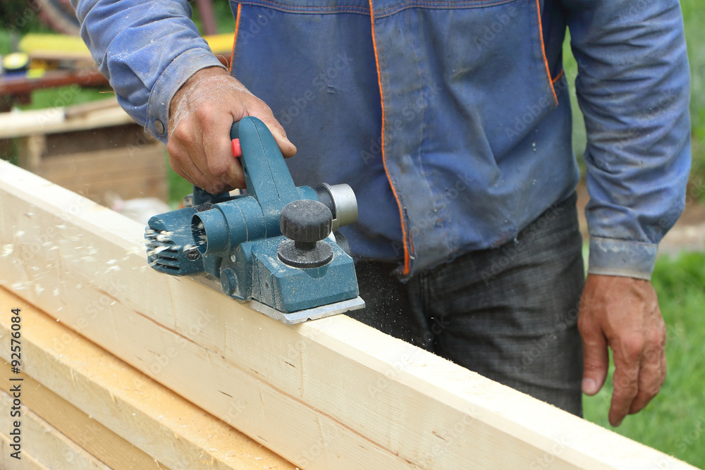 The male hand processes a wooden board an electric planer outdoors
