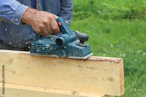 The male hand processes a wooden board an electric planer outdoors 