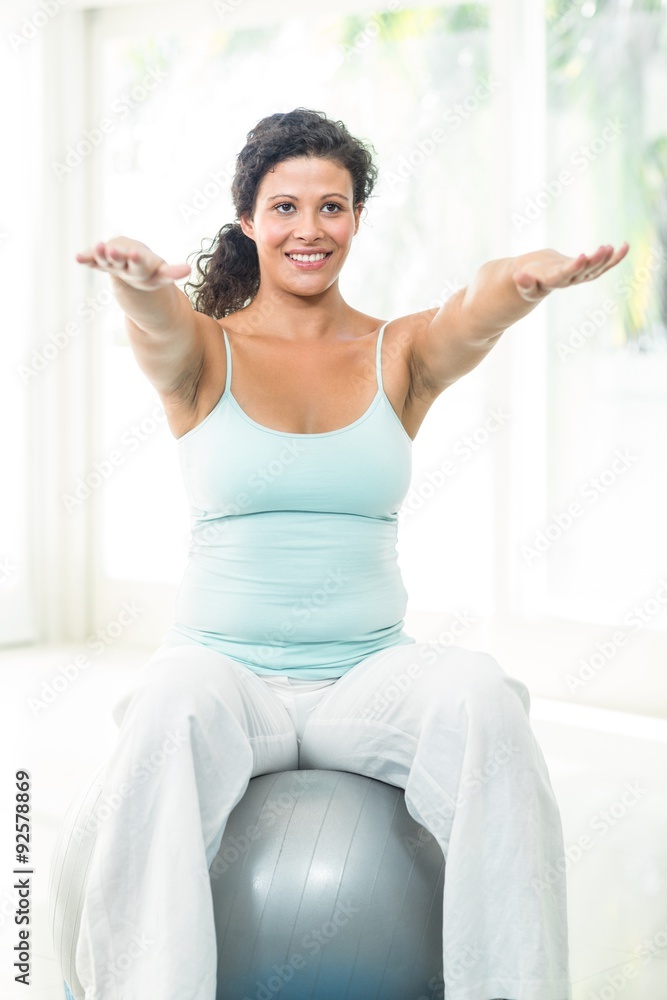 Pregnant woman with arms stretched exercising with ball