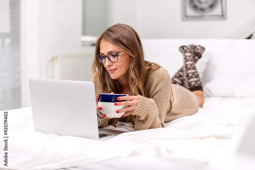 Young woman lying on bed, with coffee and laptop Young woman lying on bed, with coffee and laptop