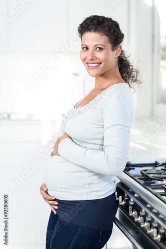 Pregnant woman touching her bellly while standing in kitchen photo