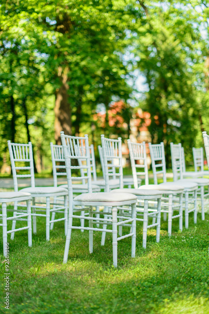White wedding chairs set up on green grass before the ceremony