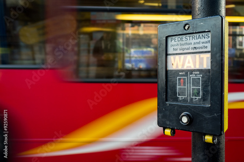 Pedestrians wait! A UK pedestrian crossing sign with a motion blurred London bus background.