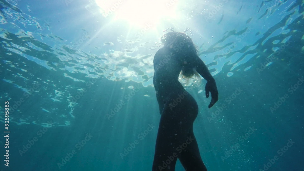 Woman in Bikini swimming underwater towards surface with beautiful sun flares. Instagram Color Tone Woman in Bikini swimming underwater towards surface with beautiful sun flares. Instagram Color Tone