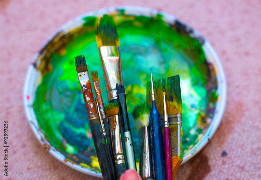 Fototapeta premium Paint brushes in man hand to the painting palette with colors 