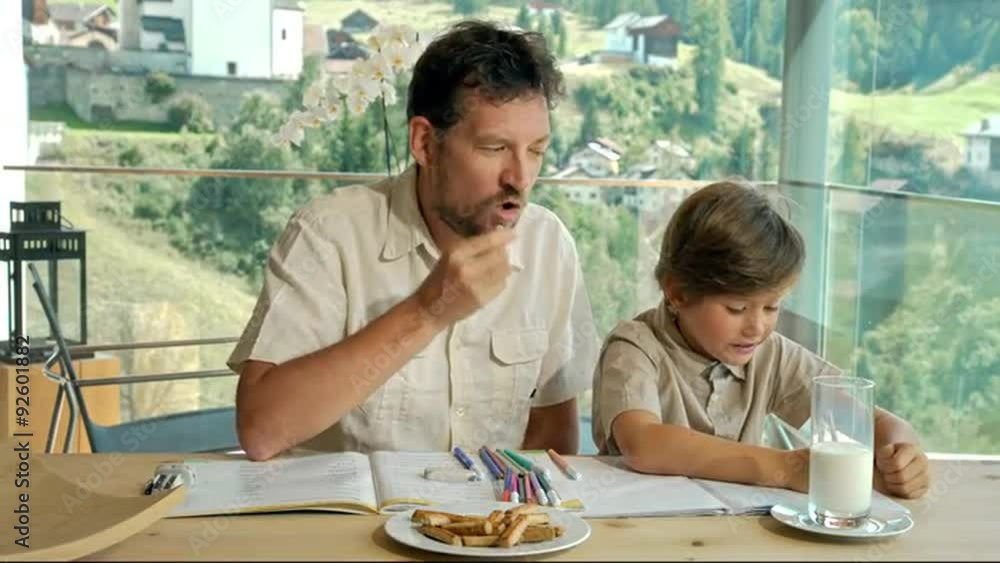 Father helping son doing homework eating snacks Father helping son doing homework eating snacks
