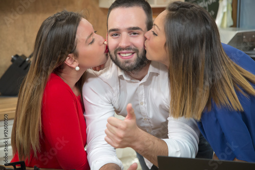Photos Two women kissing a happy man on the cheek.